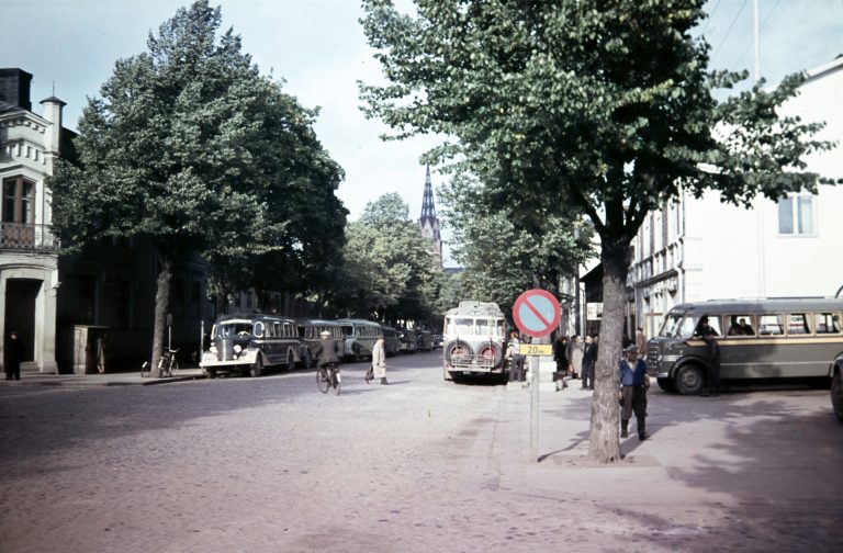 Katunäkymä, jossa vanhoja linja-autoja ja kevyttä liikennettä.